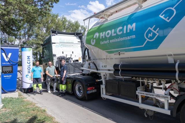 Elektrischer Mercedes-Benz eActros 600 mit Holcim-Silosattelauflieger an einer Ladestation in Mannersdorf, daneben drei Mitarbeiter.