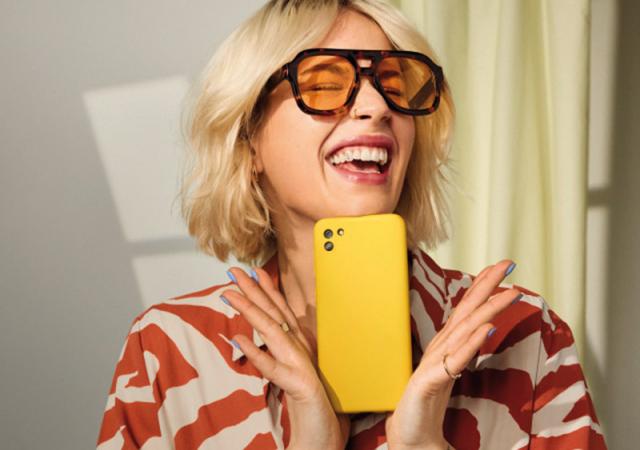 Junge Frau mit gelbem Handy jubelt